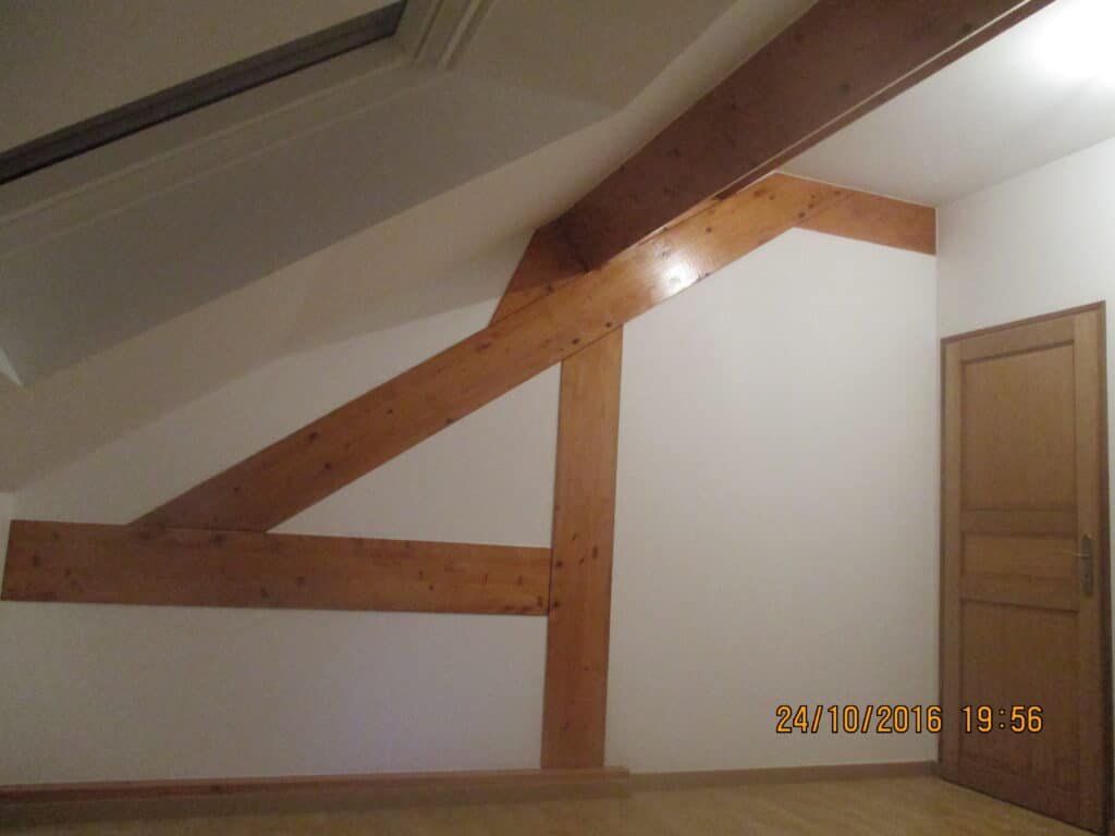 Pièce mansardée avec poutres apparentes et porte en bois
