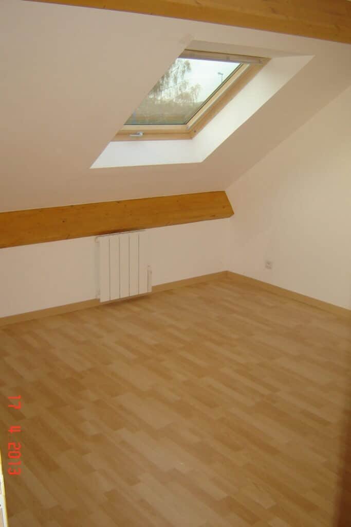 Chambre mansardée avec parquet clair et fenêtre de toit