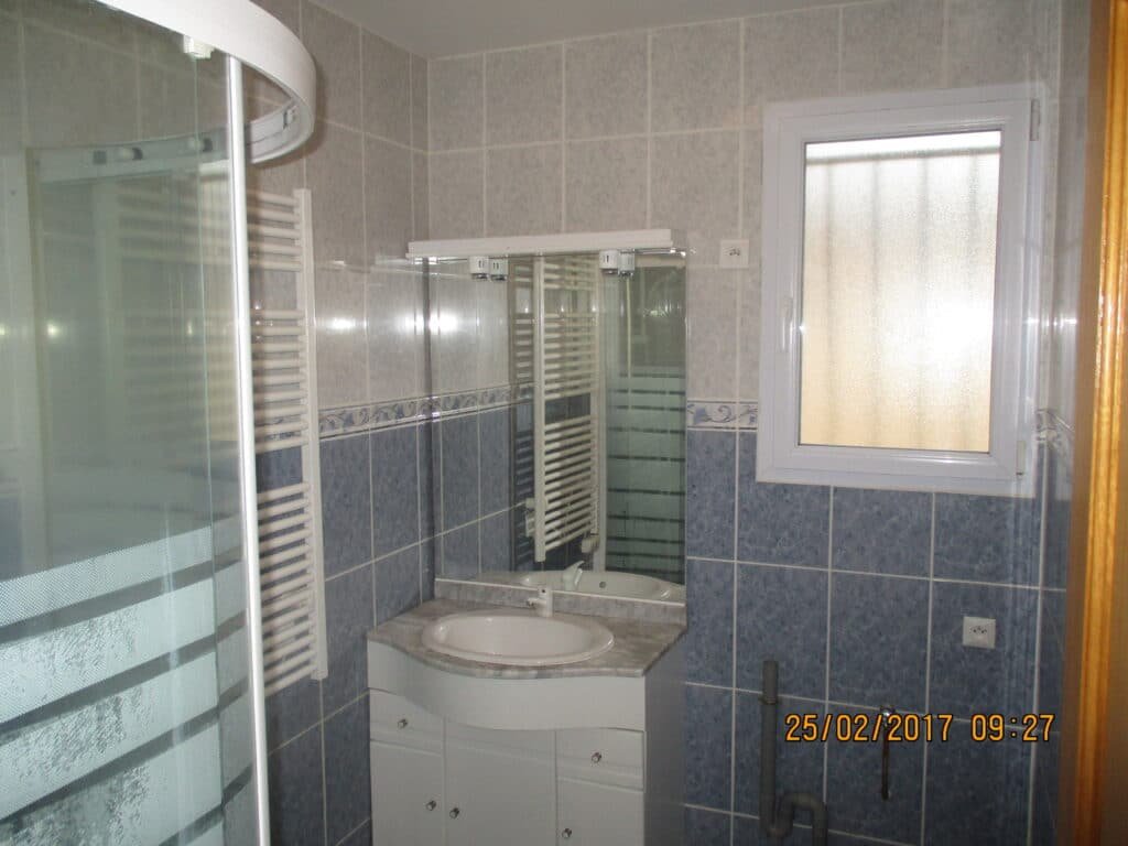 Salle de bain carrelée avec douche vitrée et meuble vasque