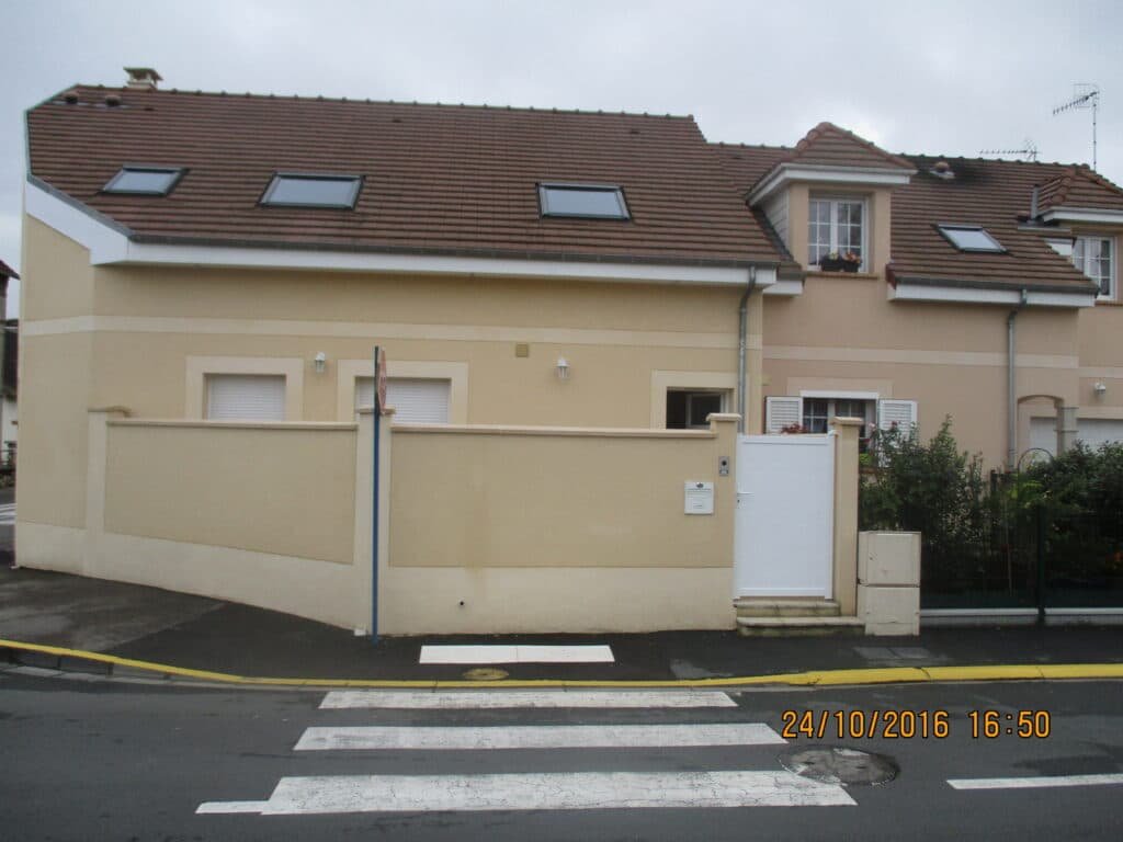 Maison beige avec mur d'enceinte assorti, en bord de rue résidentielle