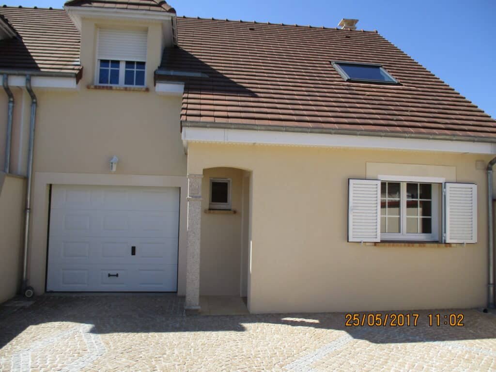 Façade de maison beige avec garage intégré et volets blancs