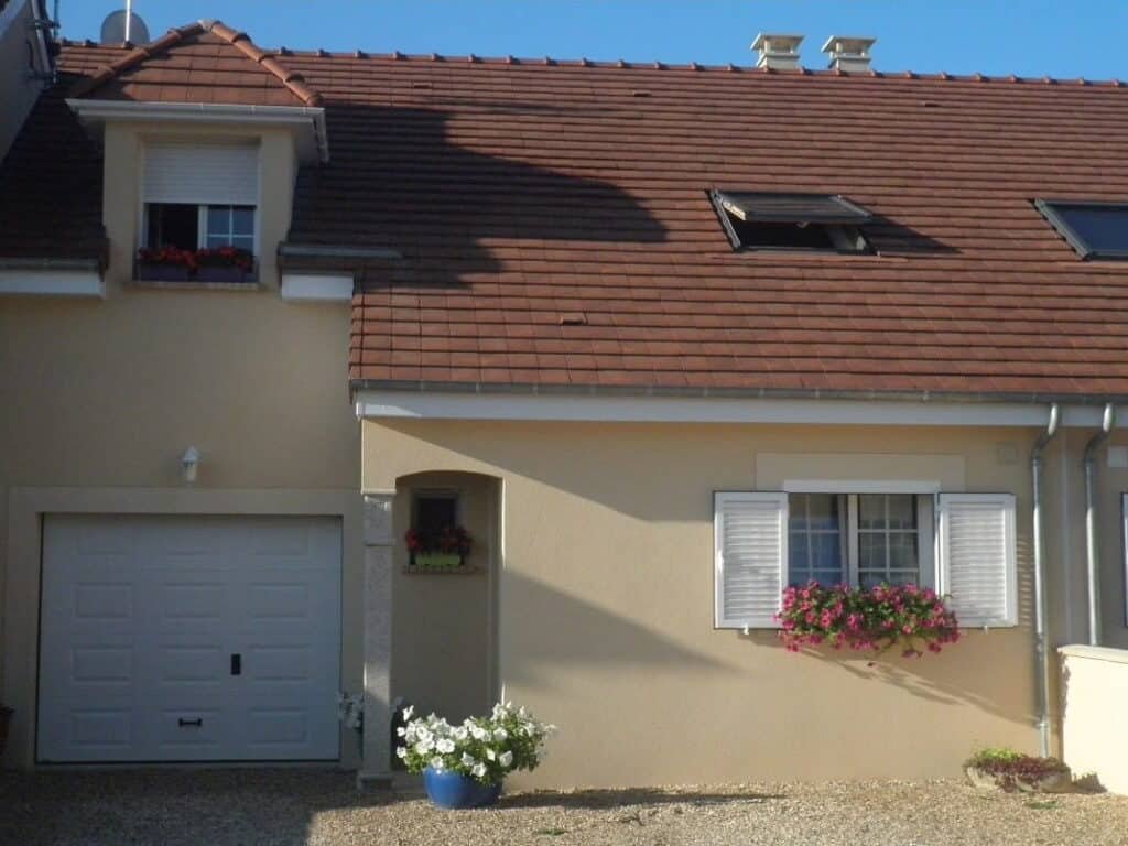 Façade de maison beige avec volets blancs et jardinières fleuries